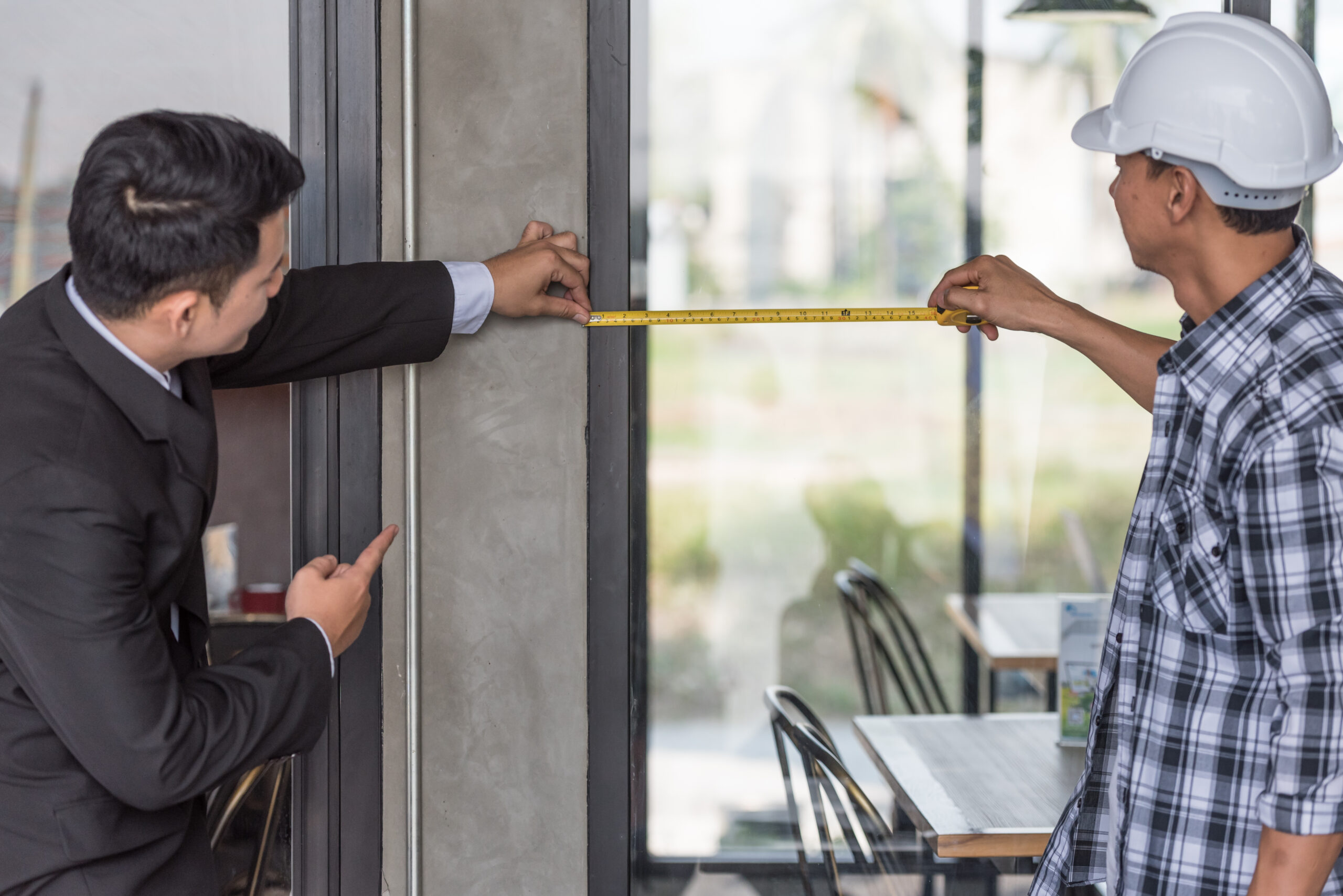 Two men taking measurements of a door for a commercial space, highlighting the importance of hiring an experienced professional who pays attention to detail for door and window installation