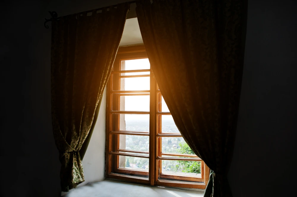 A dark room with curtains and a classic wooden window letting natural light in.