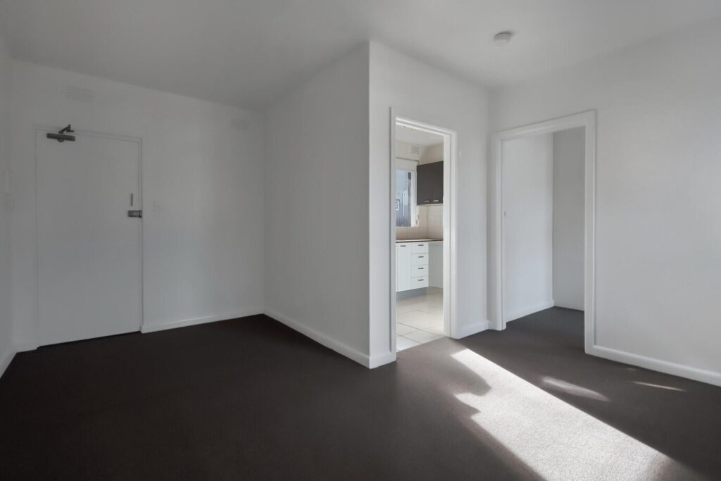 Corner of an empty room with white doors and walls and a dark floor.