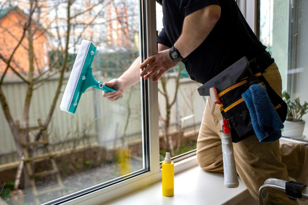 A man doing preventive maintenance on a glass window, highlighting the importance of offering good door and window services.