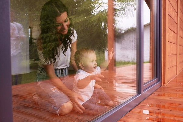 Mother and child looking out of the window comfortably indoors, representing the importance of installing energy-efficient windows and doors and maintaining a consistent temperature indoors.