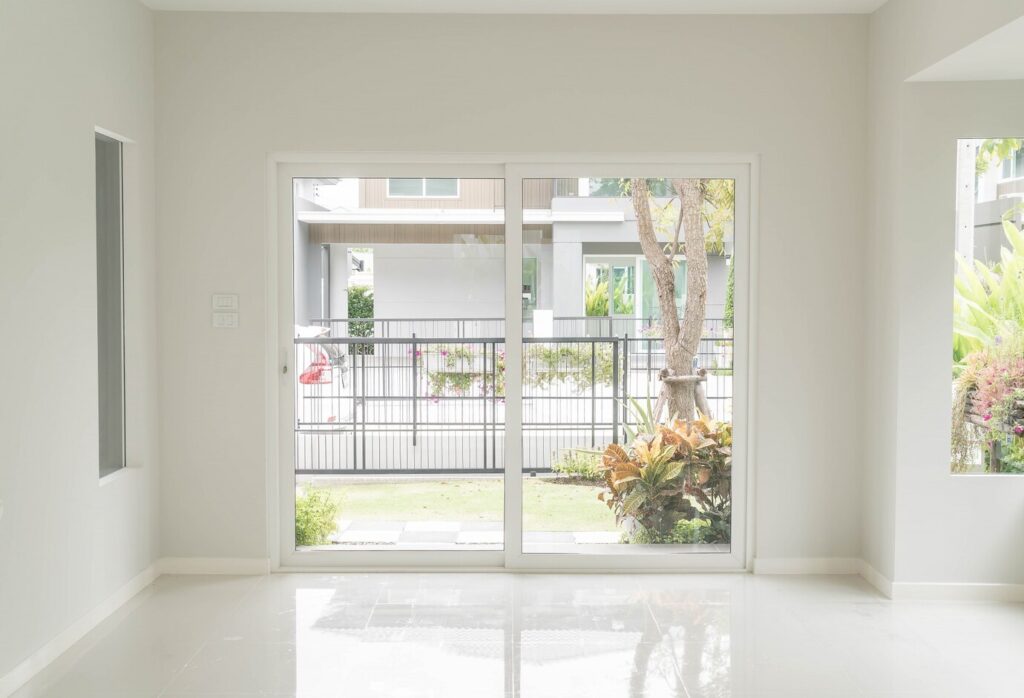 Sliding doors of an empty living room, showing the outdoor area in the background, representing the importance of choosing between sliding doors vs hinged doors.