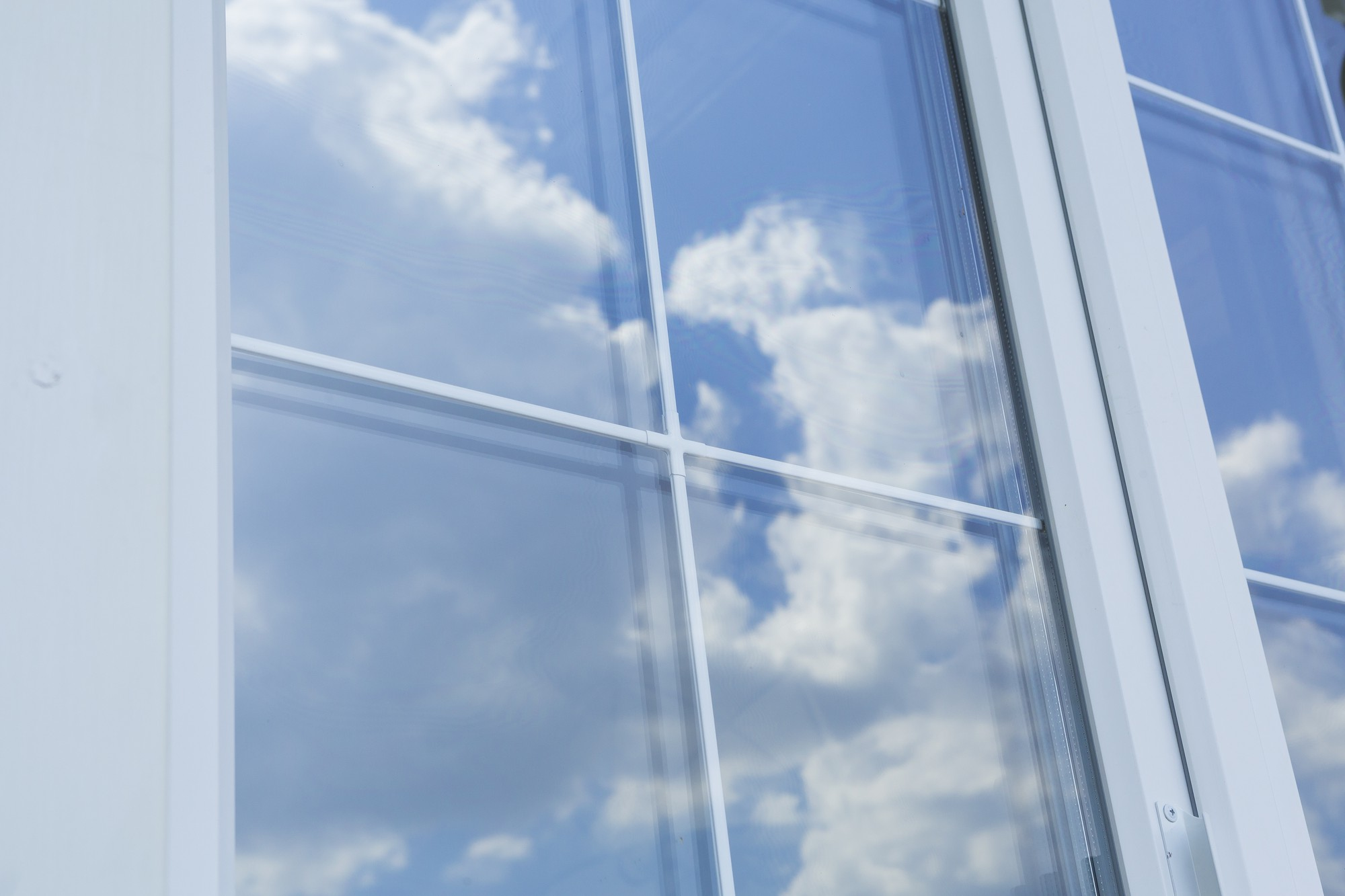 Focus on a glass window reflecting the blue sky with clouds, representing the importance of choosing the right material among the various types of glass for windows.