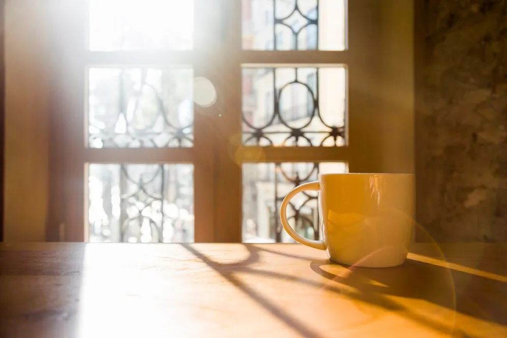 A cup of coffee on a table, illuminated by the sunlight entering the house after a window renovation to maximize natural light.