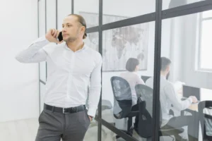 Man speaking on a cellphone beside soundproof office windows and doors.